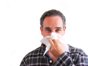 Middle aged man looking at the camera and using a tissue to blow his nose